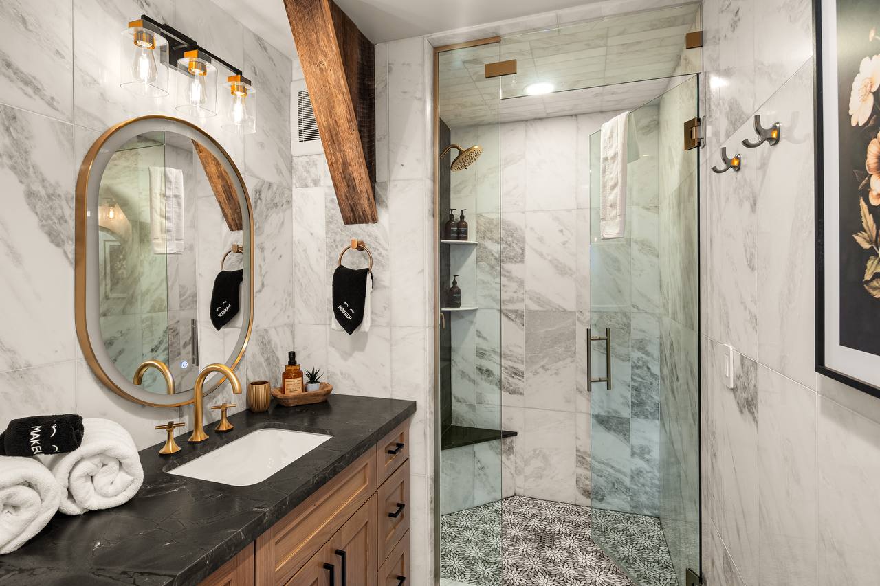Marble bathroom with gold fixtures, glass shower, and obsidian vanity